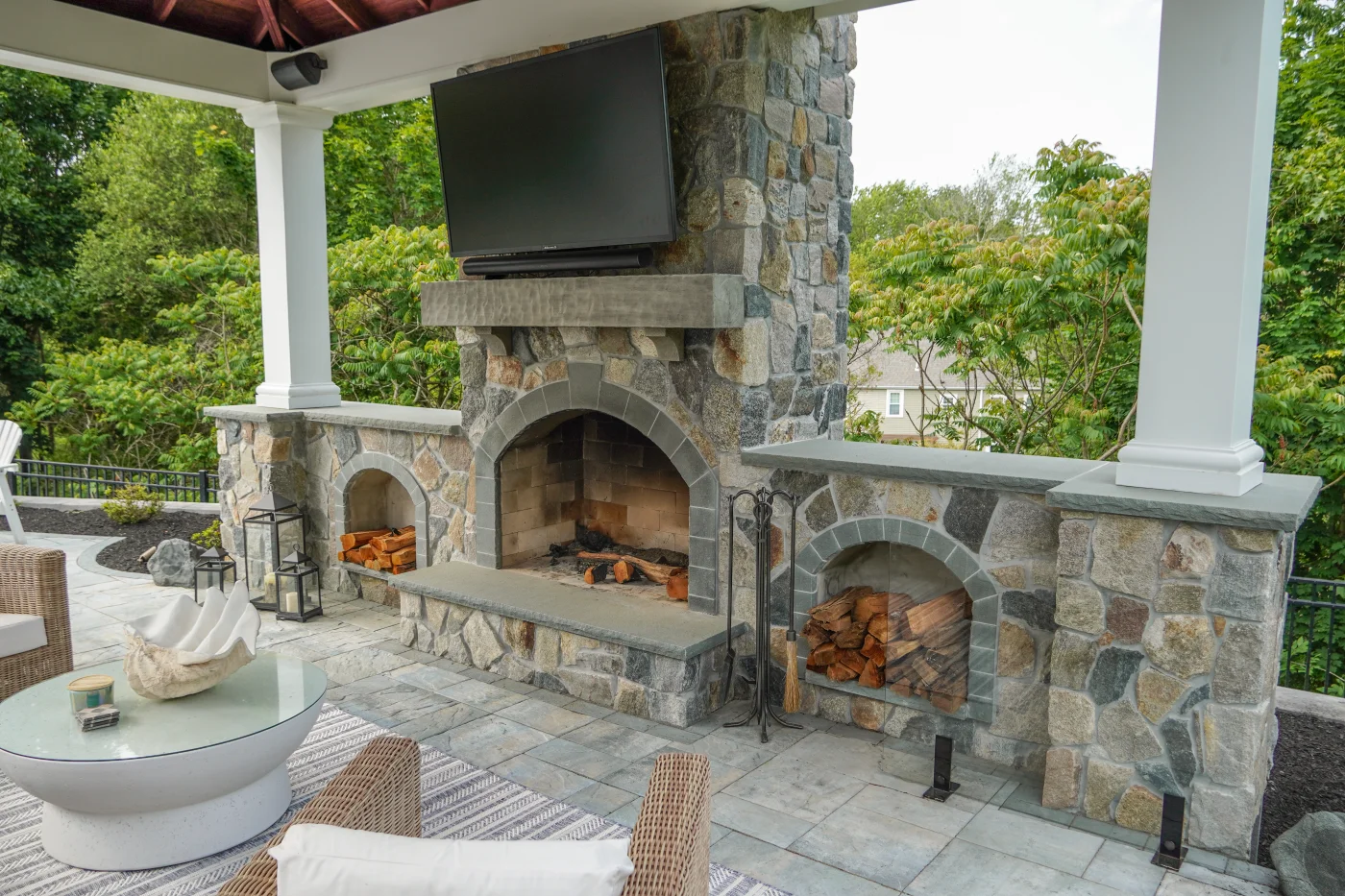 Outdoor stone fireplace with mounted TV and built-in wood storage